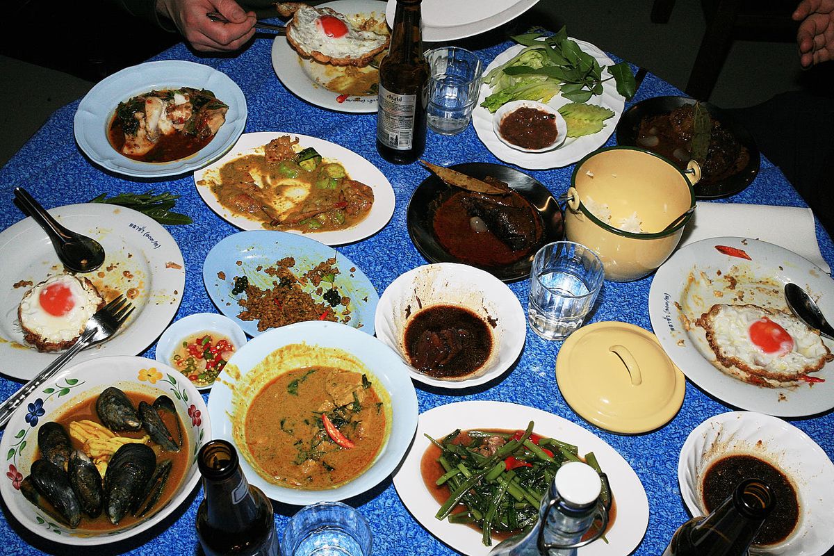 A spread of southern Thai curries, some topped with fried egg, on a blue tablecloth