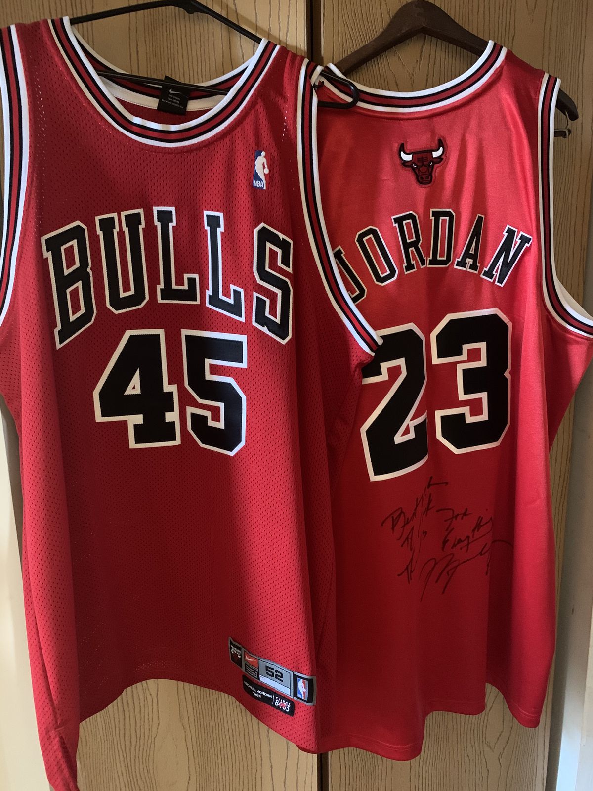 Two red basketball jerseys hanging from hangers.