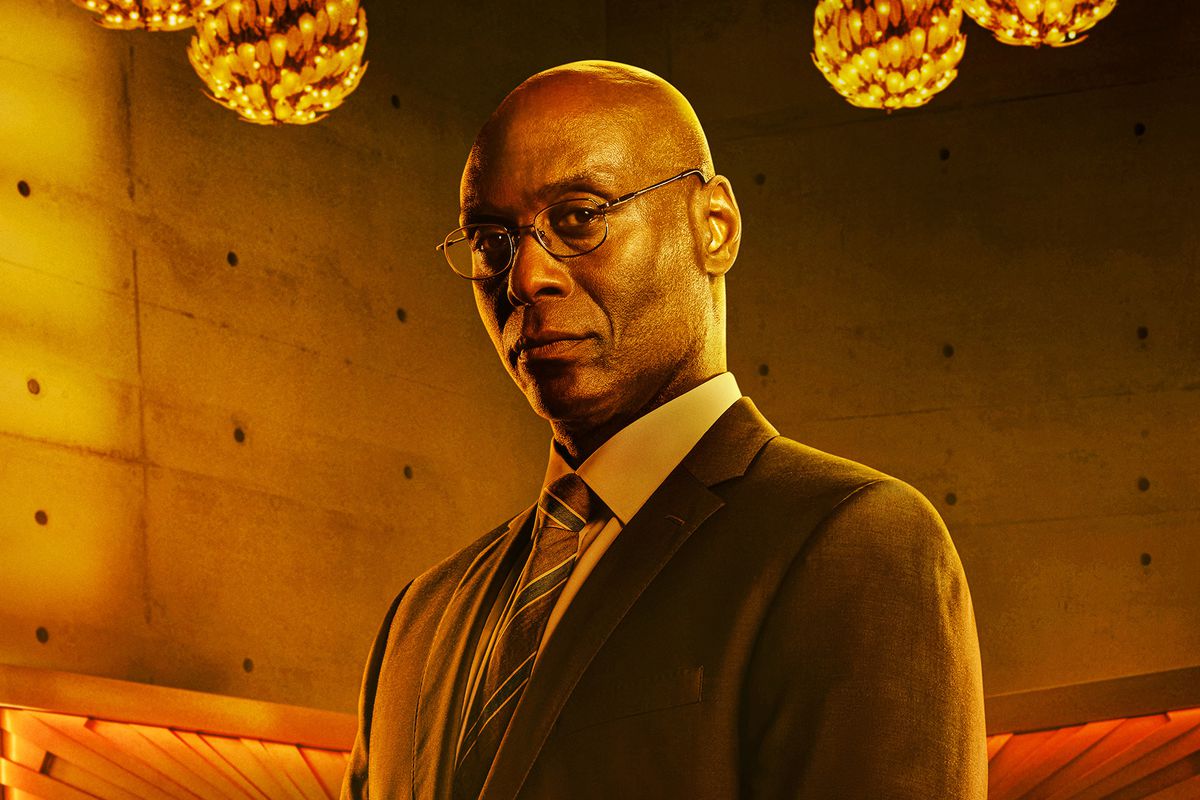 Lance Reddick, as the concierge Charon, stands solemnly in the lobby of the Continental Hotel in a dramatically orange-lit poster image for John Wick: Chapter 4
