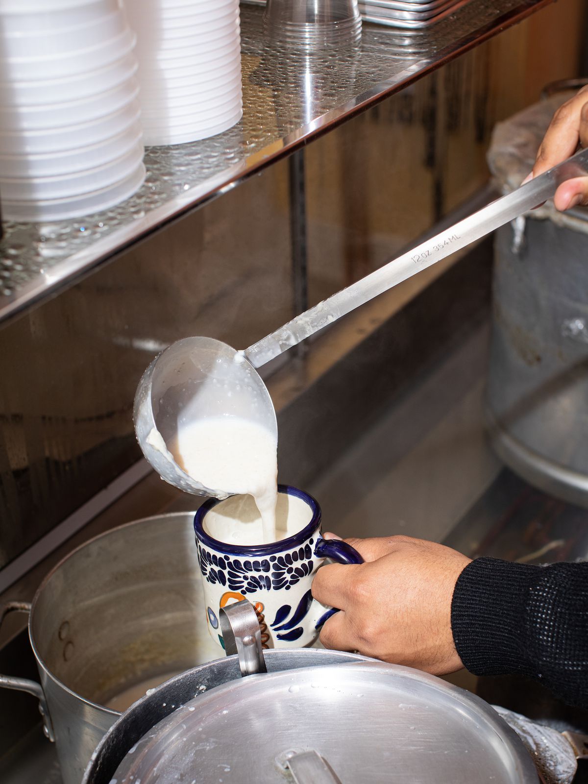 A worker holds a colorful ceramic cup and pours a thick white drink, called an atole.