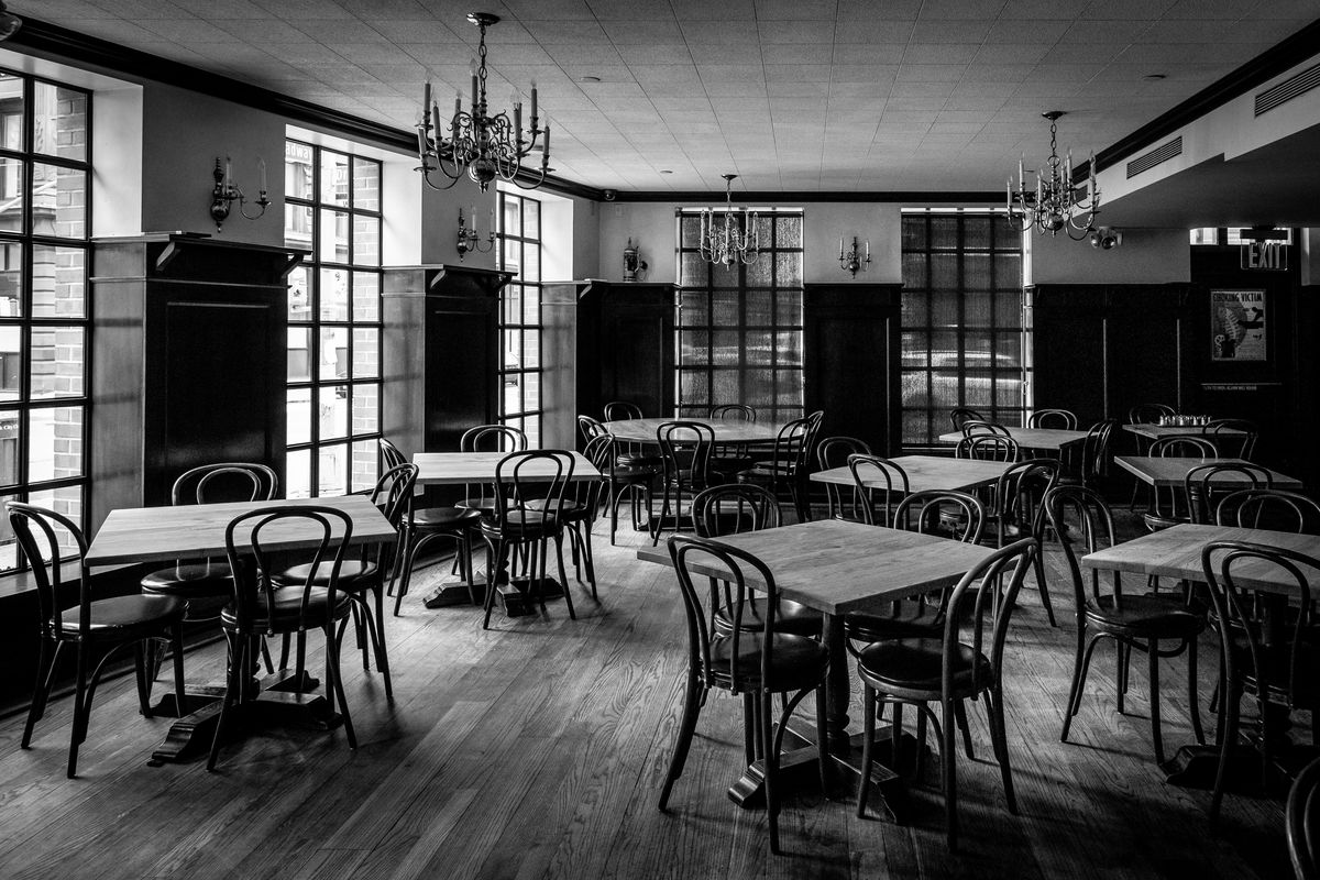 A black and white photo of an empty restaurant, with several tables-of-four