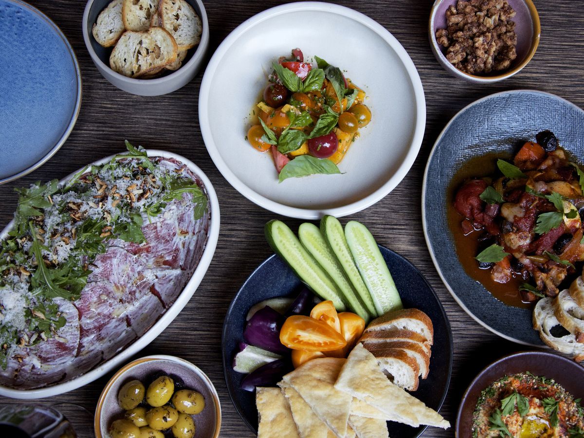 From top-down, a table filled with dishes like prosciutto salad, crudite, olives, and nust