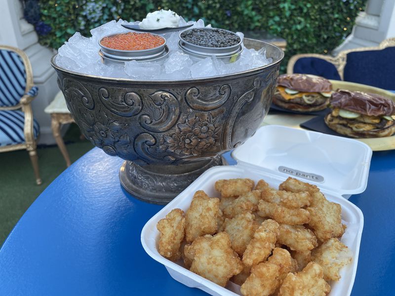 A box of tater tots, two burgers, and an ice bowl with caviar.