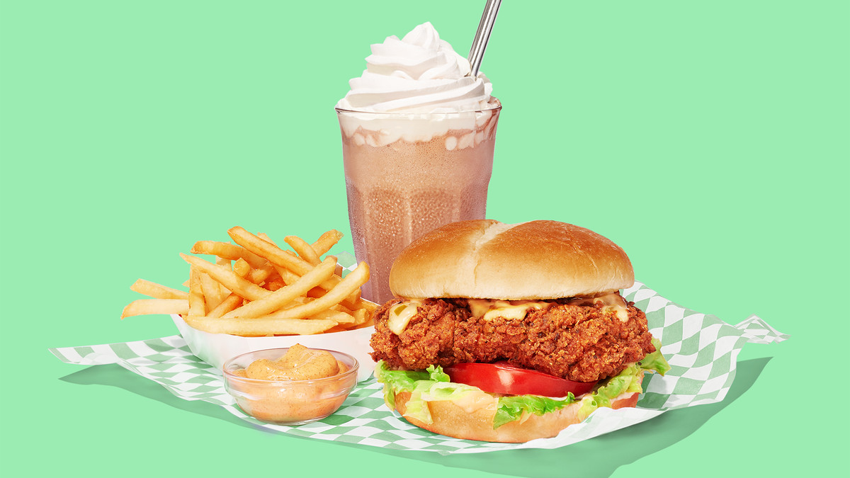 A fried chicken sandwich, fries, and a shake artfully arranged on a napkin.