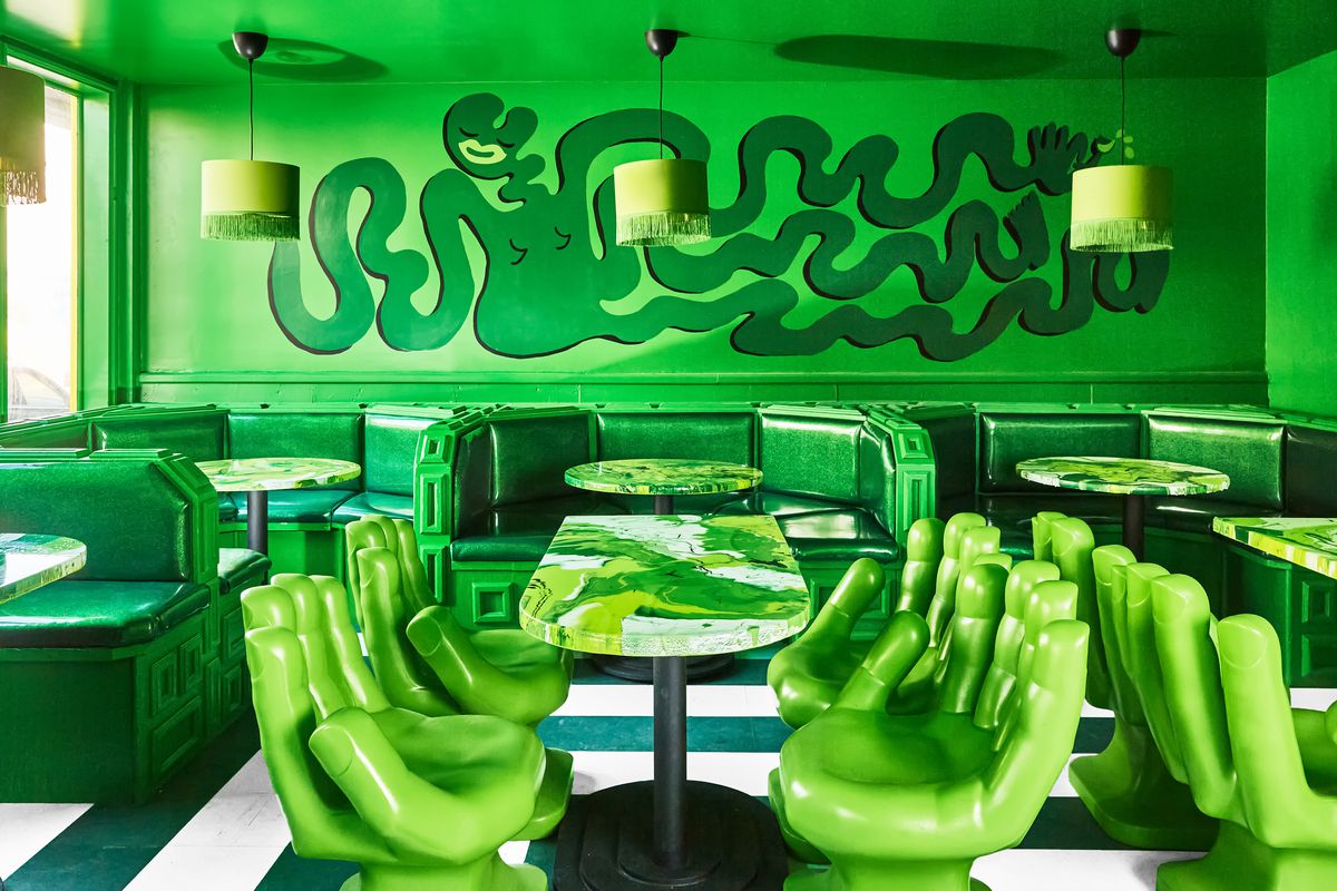 A green room, with large hand-shaped chairs, and a swirling figure on the wall.