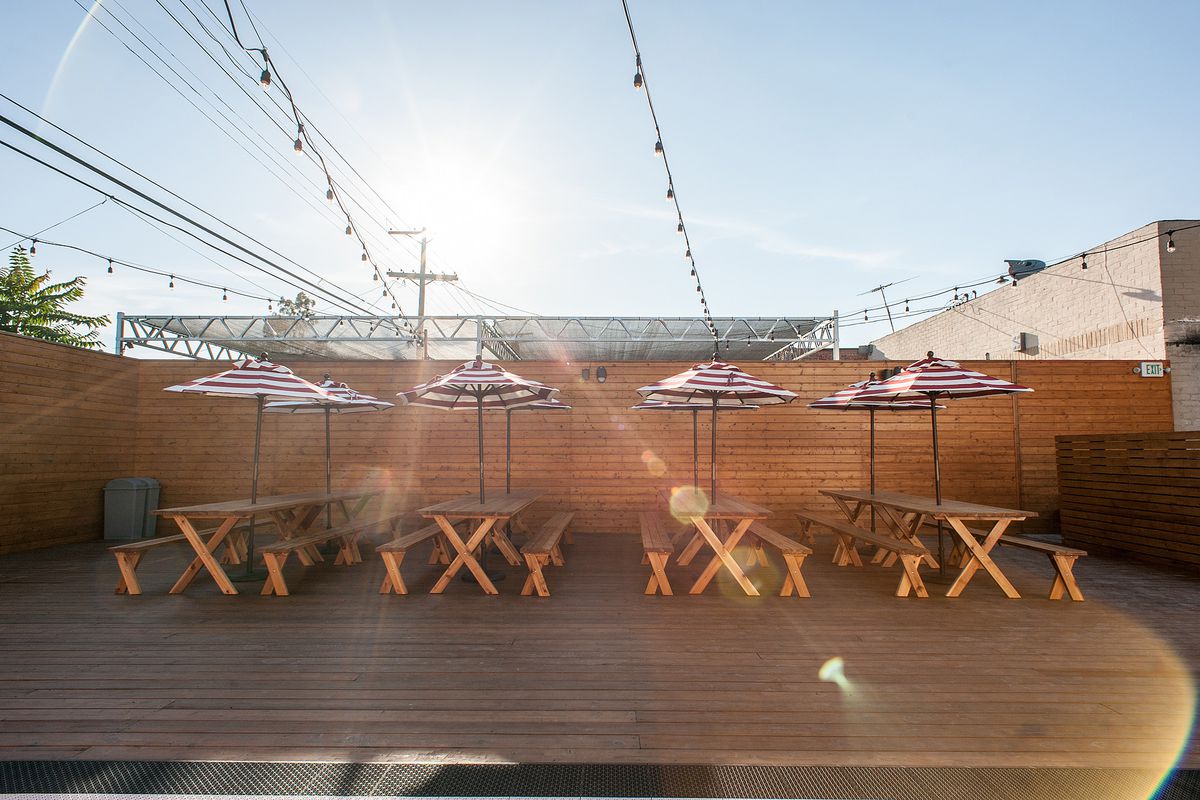 A wooden outdoor space with sun streaming over umbrellas at daytime.