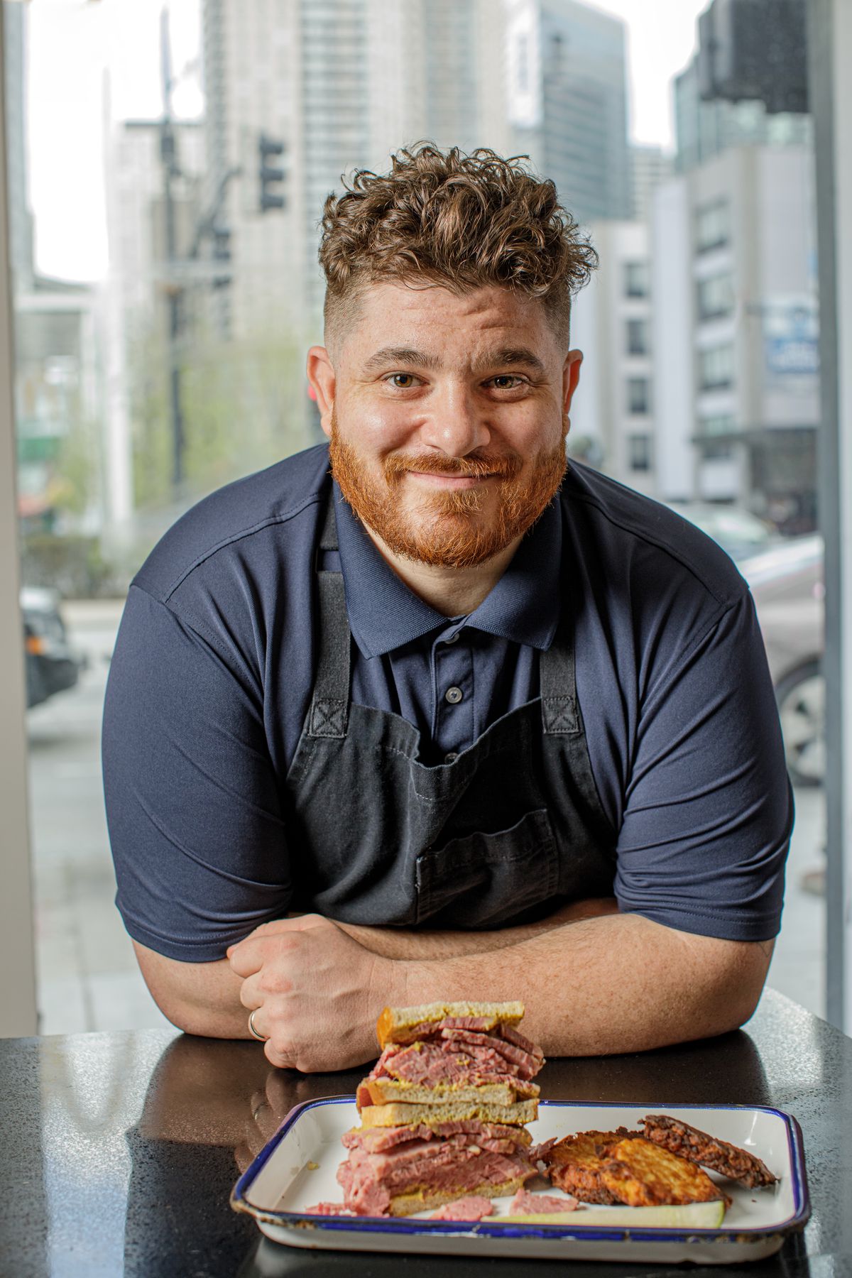 A man in an apron poses and smiles.