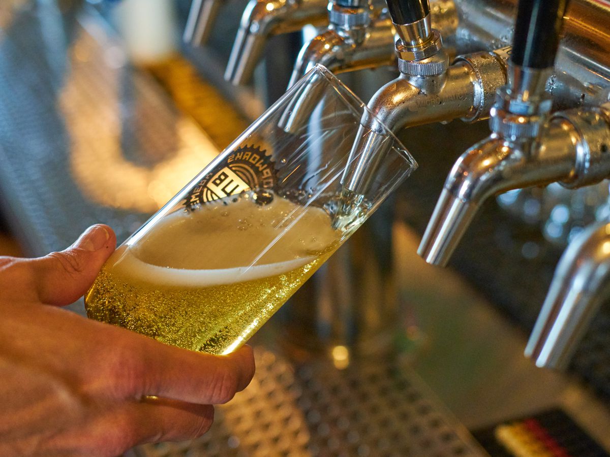 A light colored beer pouring from a tap into tall, clear glass. 