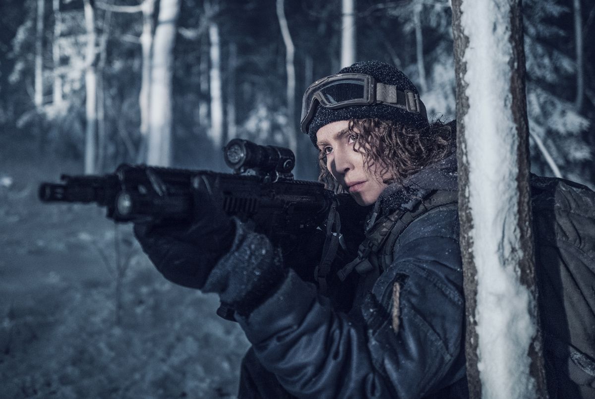 Noomi Rapace aims her rifle in a wintry wood