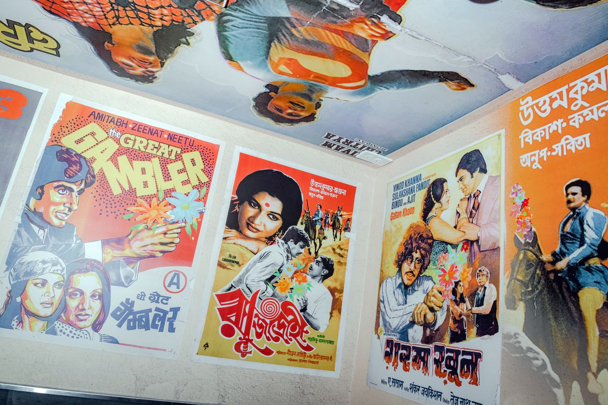 Bright and colorful movie posters cover the walls and ceiling of a restaurant bathroom.