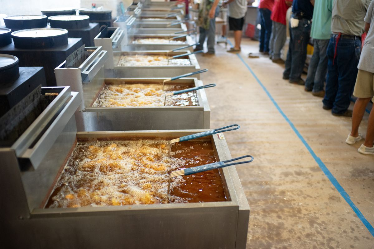 A line of a half-dozen fryers containing boiling oit and fry baskets.