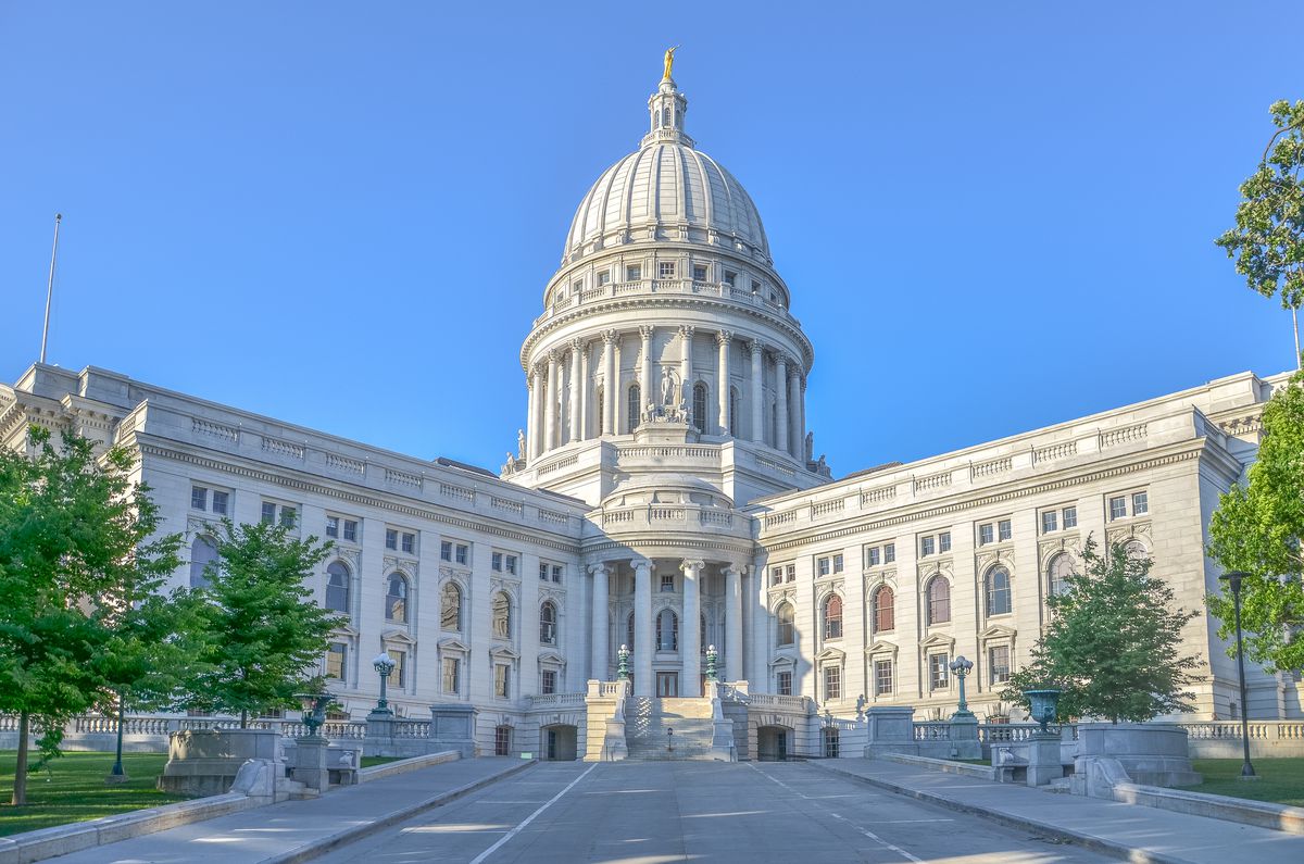 The exterior of the Wisconsin State Capitol. The facade is white. There is a large domed tower. There are columns flanking the entryway. 