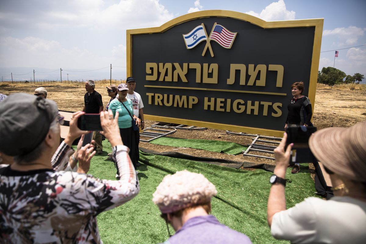 People take photos of a large sign with “Trump Heights” written in English underneath Hebrew writing and the US and Israel flags at the top.