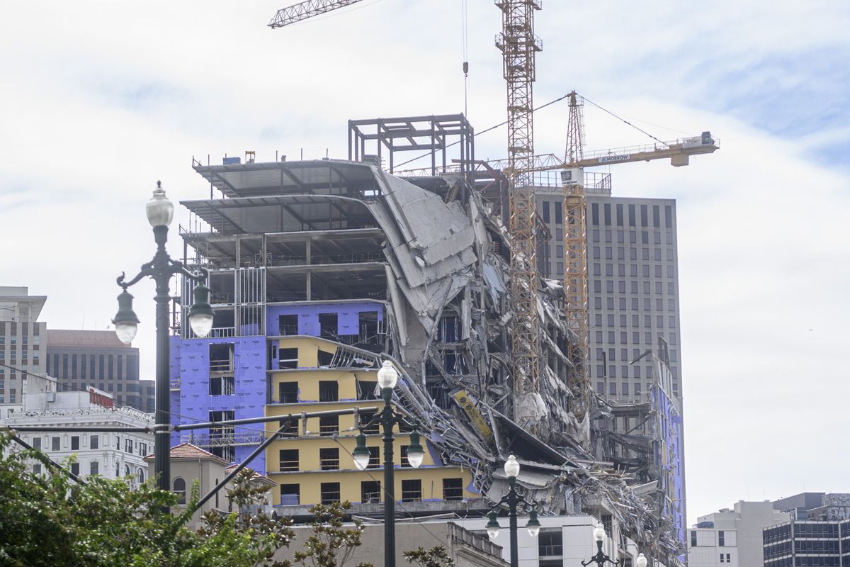 A collapsed hotel with two large cranes hovering above it faces Canal Street