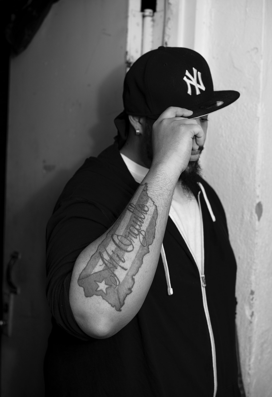 A man with a New York Yankees hat showing off a tattoo on his arm that has the Puerto Rican flag with letters on top of it that read “mi orgullo” or “my pride.” 