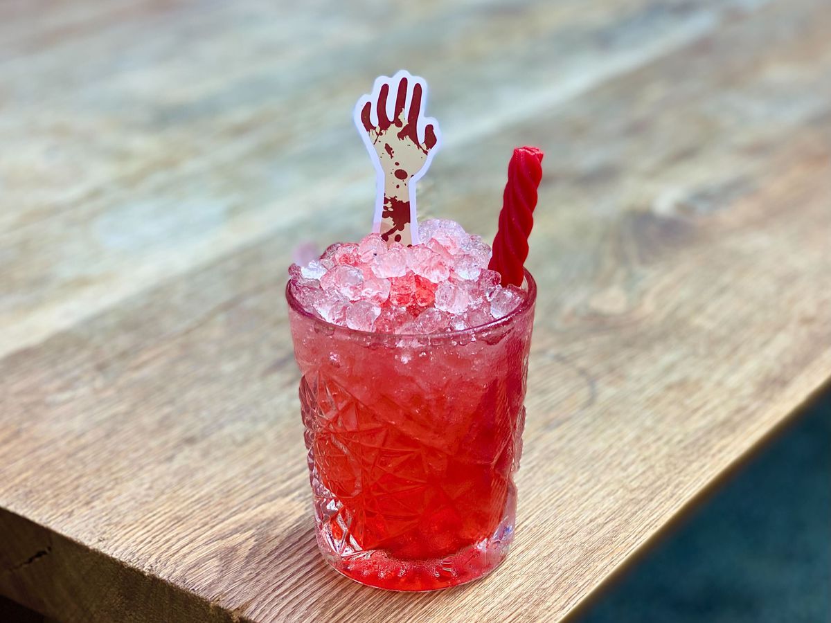 A red cocktail in a glass with Red Vine candy and paper zombie hand garnishes.