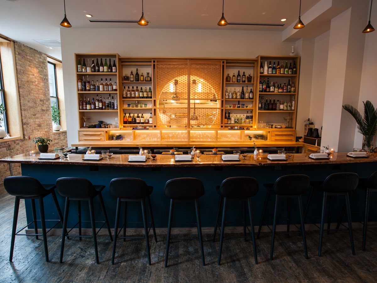 A small bar with stools in front and bottles on shelves behind