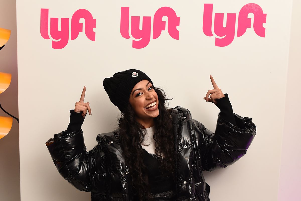 A woman smiles and points both hands over her head at the Lyft logo.
