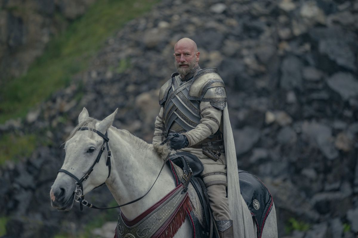 Ser Harrold Westerling, con su armadura, se sienta sobre su caballo blanco frente a una colina rocosa en House of the Dragon.