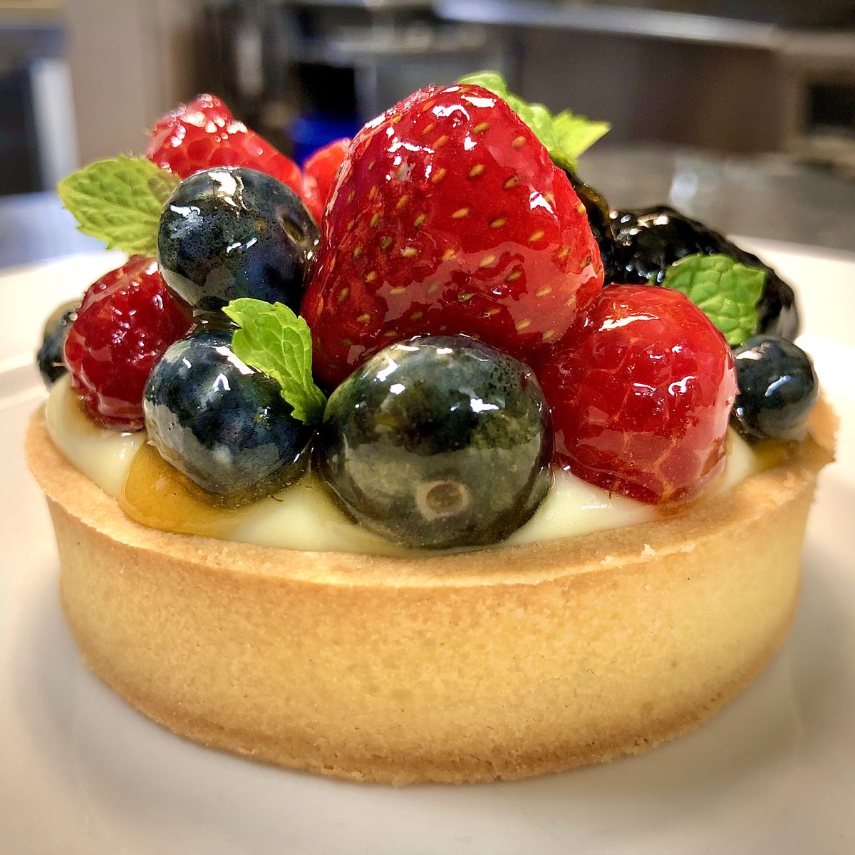 A custard filled pastry tart topped strawberries, blueberries, and mint
