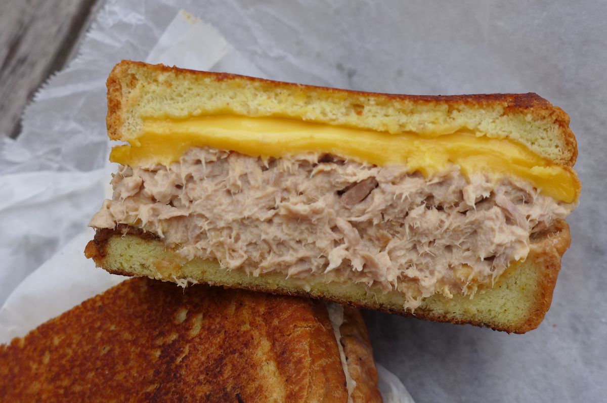 A squarish tuna melt cut in half showing yellow cheese and beige tuna salad oozing mayo.