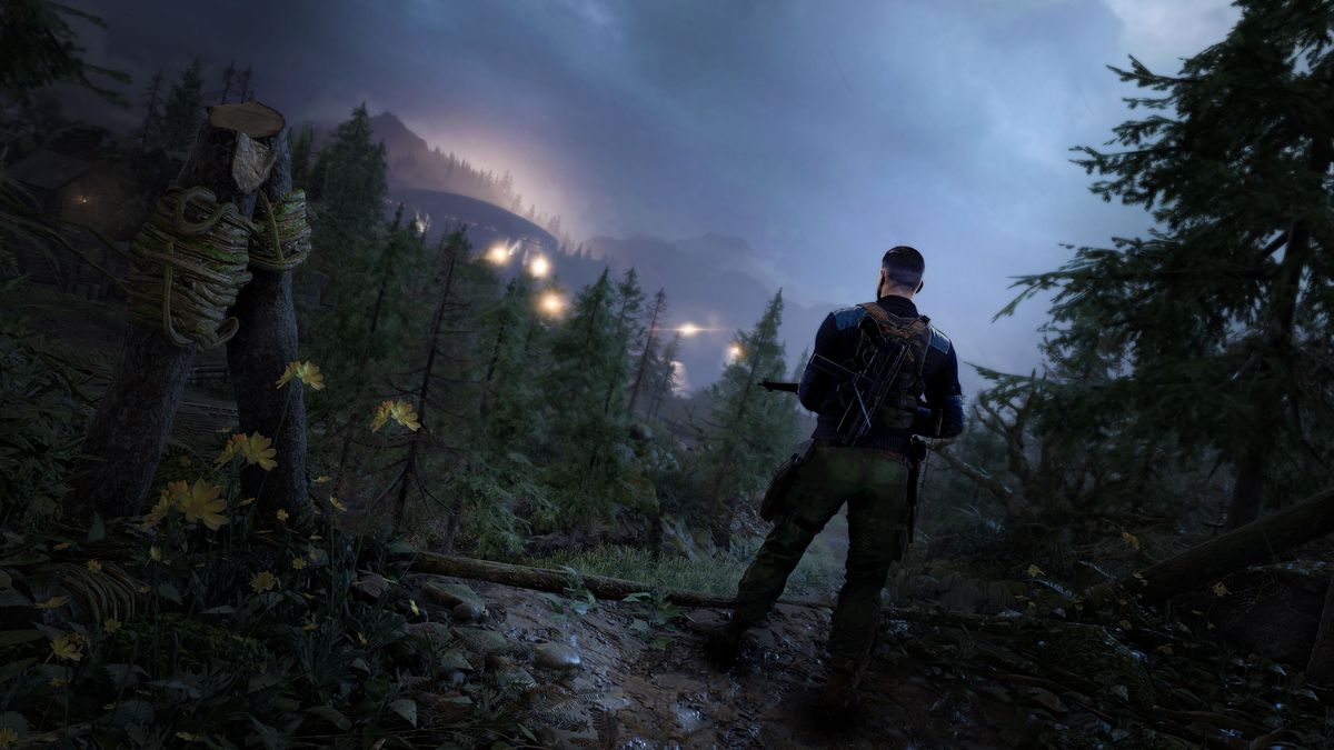 A Nazi soldier, back to the viewer, stands guard in a dark, wooded area of Sniper Elite 5