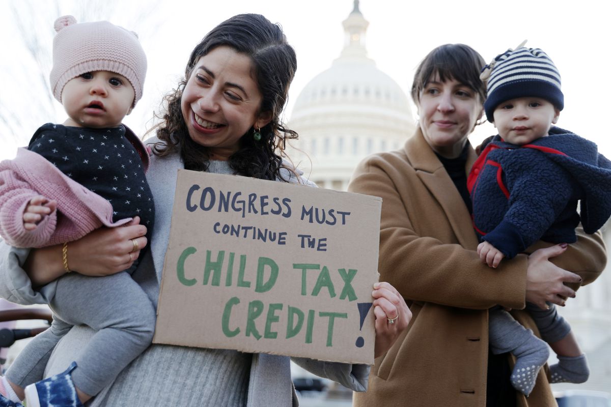 Dos madres se paran, cada una con un bebé.  Una mujer lleva un cartel que dice “¡El Congreso debe continuar con el crédito fiscal por hijos!”.