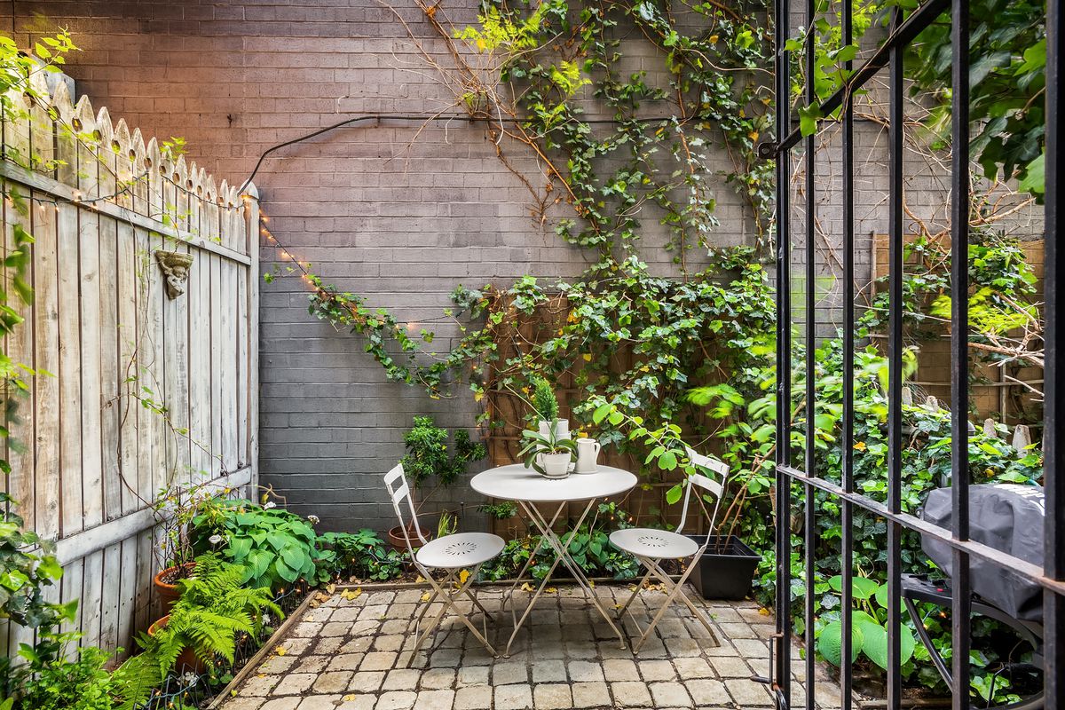 A small patio with a round table and two chairs, ivy-covered wood fencing, and brick tiles.