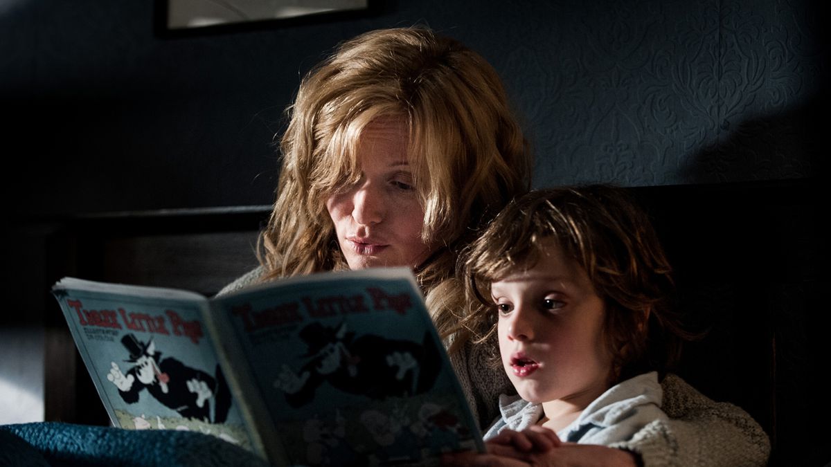 Harried single mother Amelia (Essie Davis) reads a Three Little Pigs picture book to her young son Noah (Noah Wiseman) as they lie in bed together in a dark room in a scene from The Babadook