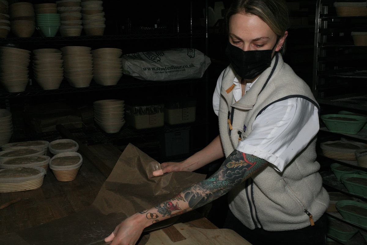 A woman moves a sack of flour in a commercial bakery.