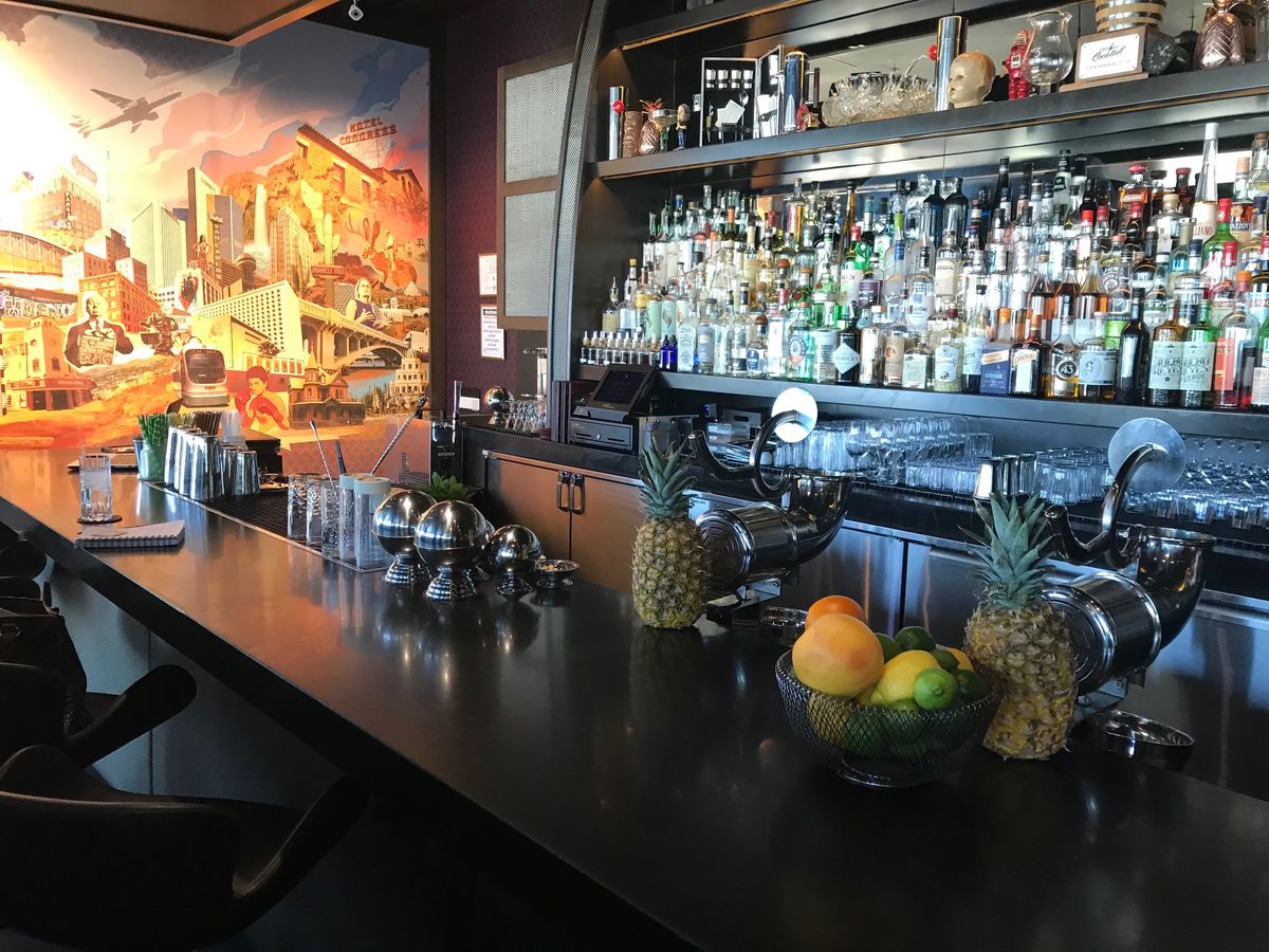 An orange and yellow mural next to a bar counter with a bowl of citrus and fresh pineapples on top.