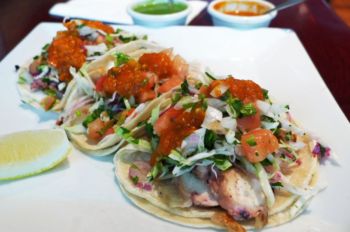 Three octopus tacos covered with shredded vegetable matter and topped with bright red salsa...