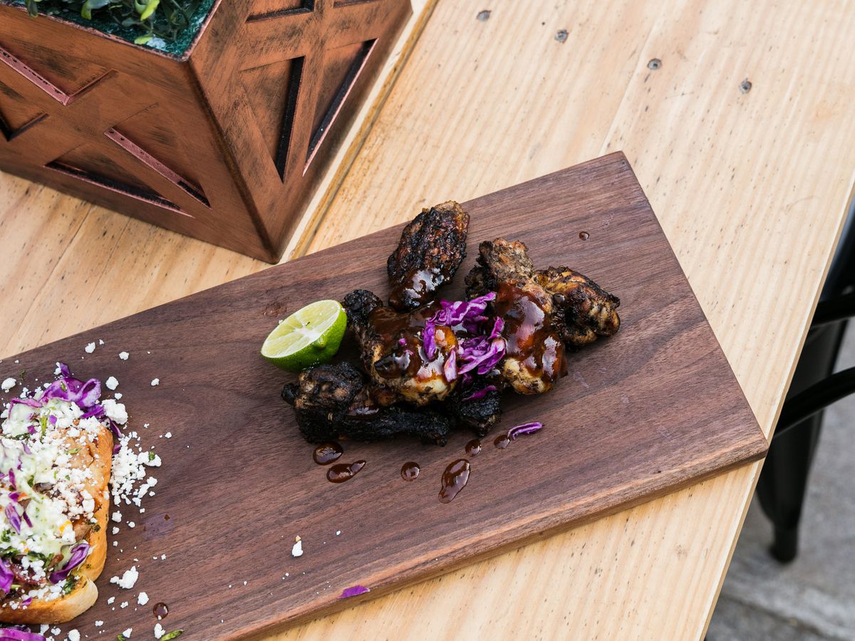 Jerk chicken wings piled on a wood plank with shredded red cabbage and a slice of lime from Coop at Detroit Shipping Company.