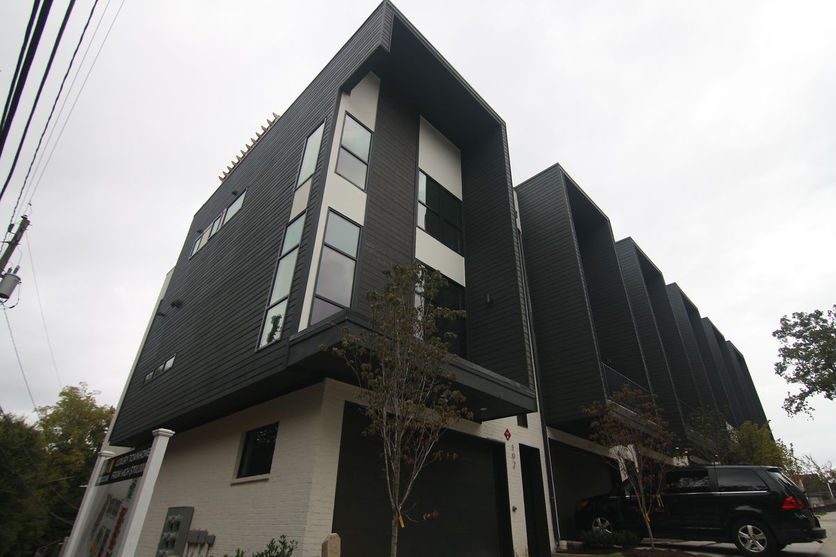 A tall black and white townhome with modern style that’s missing it’s front balcony railings.