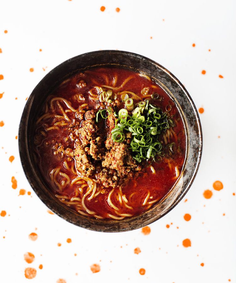 A bowl of fiery red broth with noodles and a pile of crumbled meat on top