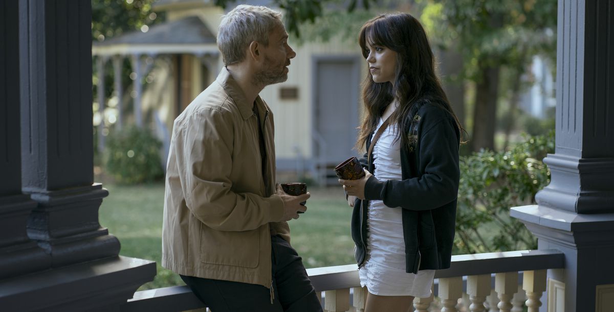 Jon Miller (Martin Freeman) and his teenage student Cairo Sweet (Jenna Ortega) stand outdoors on a veranda-style porch, talking with each other, in Miller’s Girl