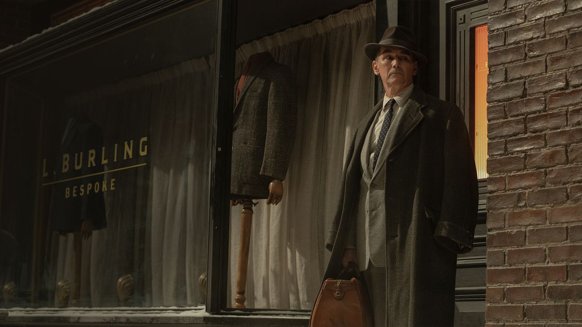 Mark Rylance as Leonard in a suit and coat standing outside of his corner tailor shop in The Outfit (2022).