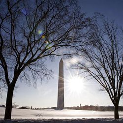 The sun shines on the snow covered ground of the Washington Monument in Washington, Thursday.