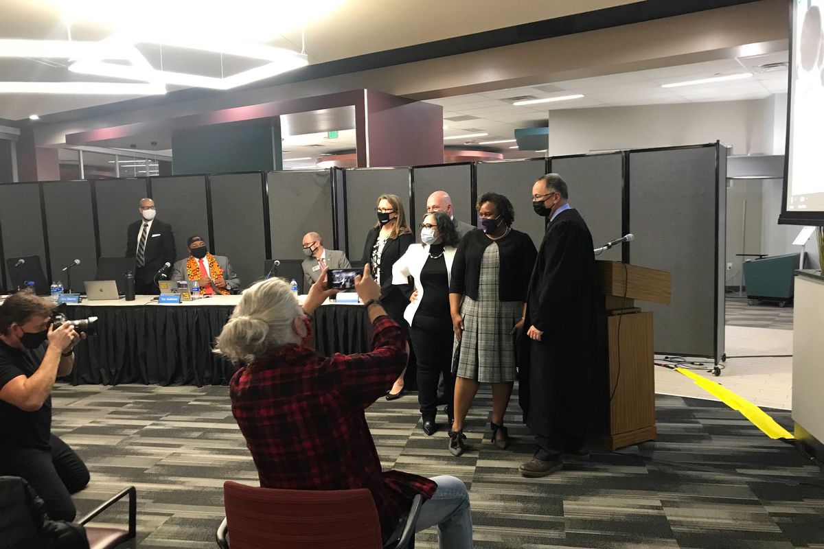 Denver school board members pose for a photo in front of a podium. People in the audience hold up cell phones to take photos.