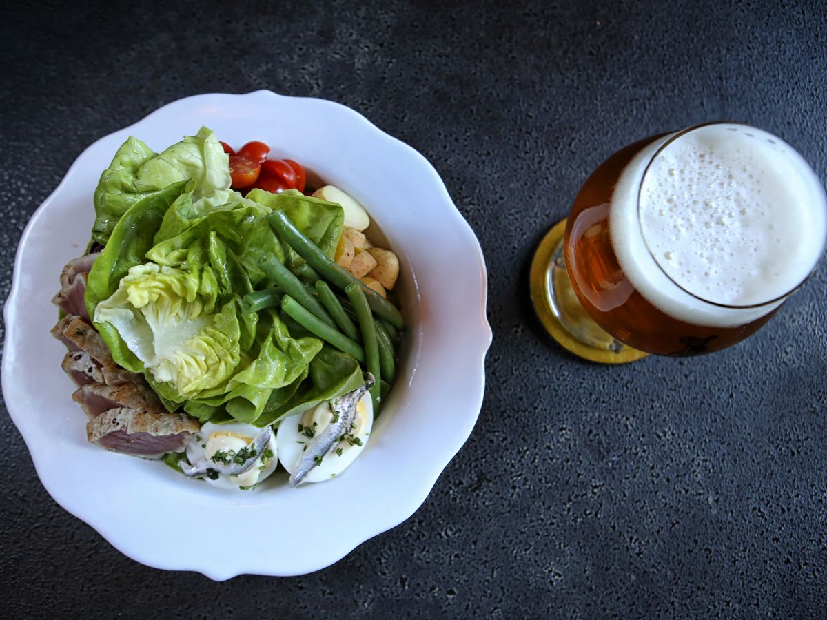 A wide white bowl of salad next to a glass of beer.