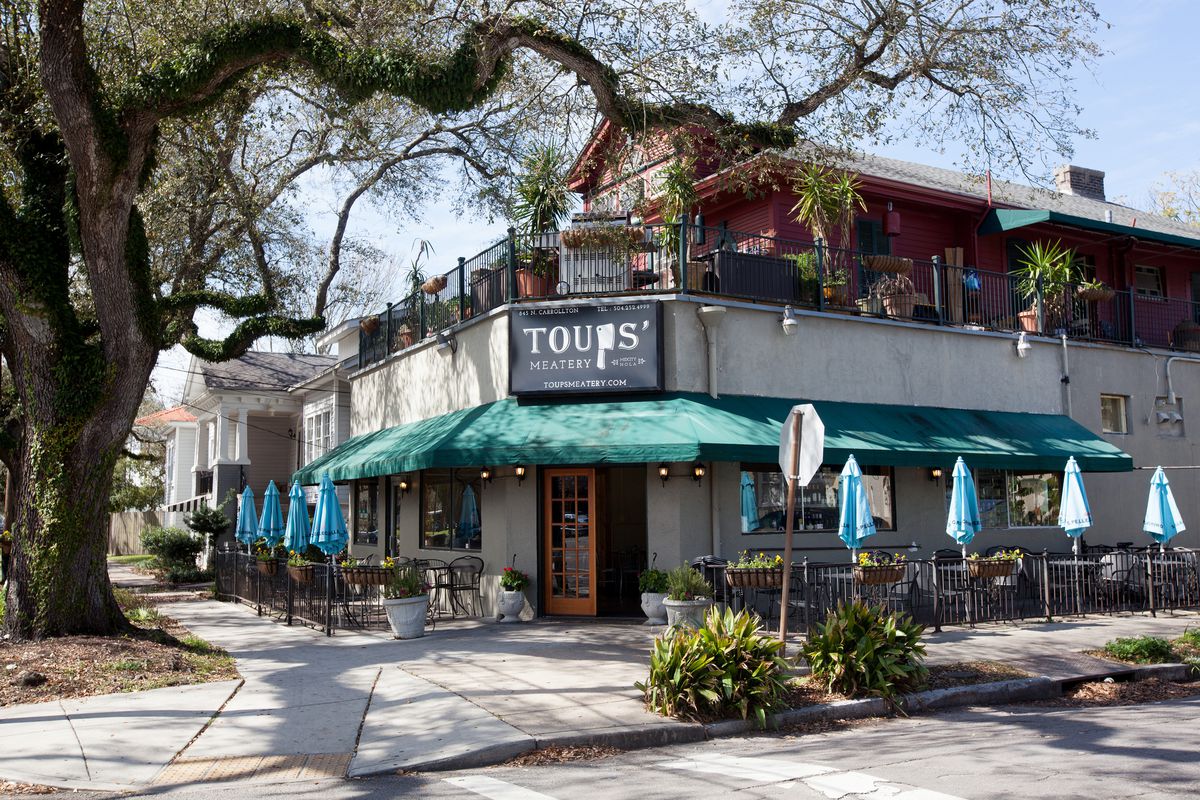 Exterior of restaurant on corner with green awnings, outdoor tables with blue umbrellas, and a Toups’ Meatery sign