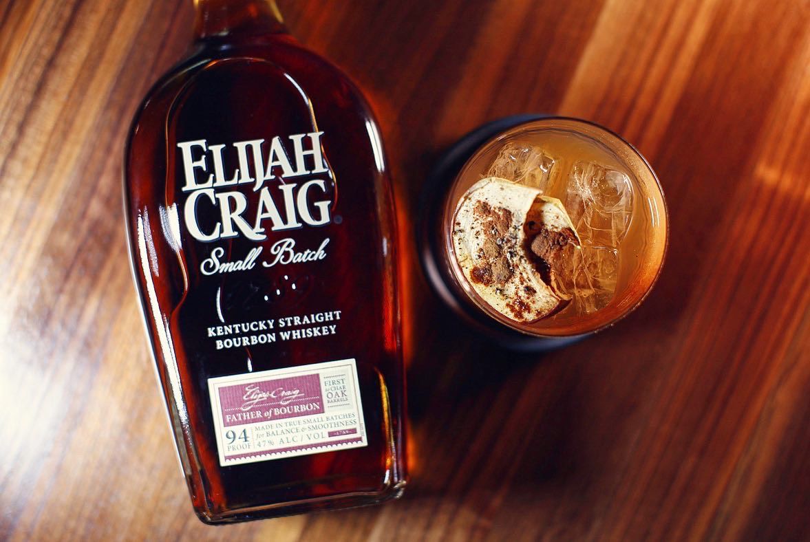 A bottle of Kentucky straight Elijah Craig whiskey next to a glass of the old-fashioned mixed with pumpkin spice, on the rocks