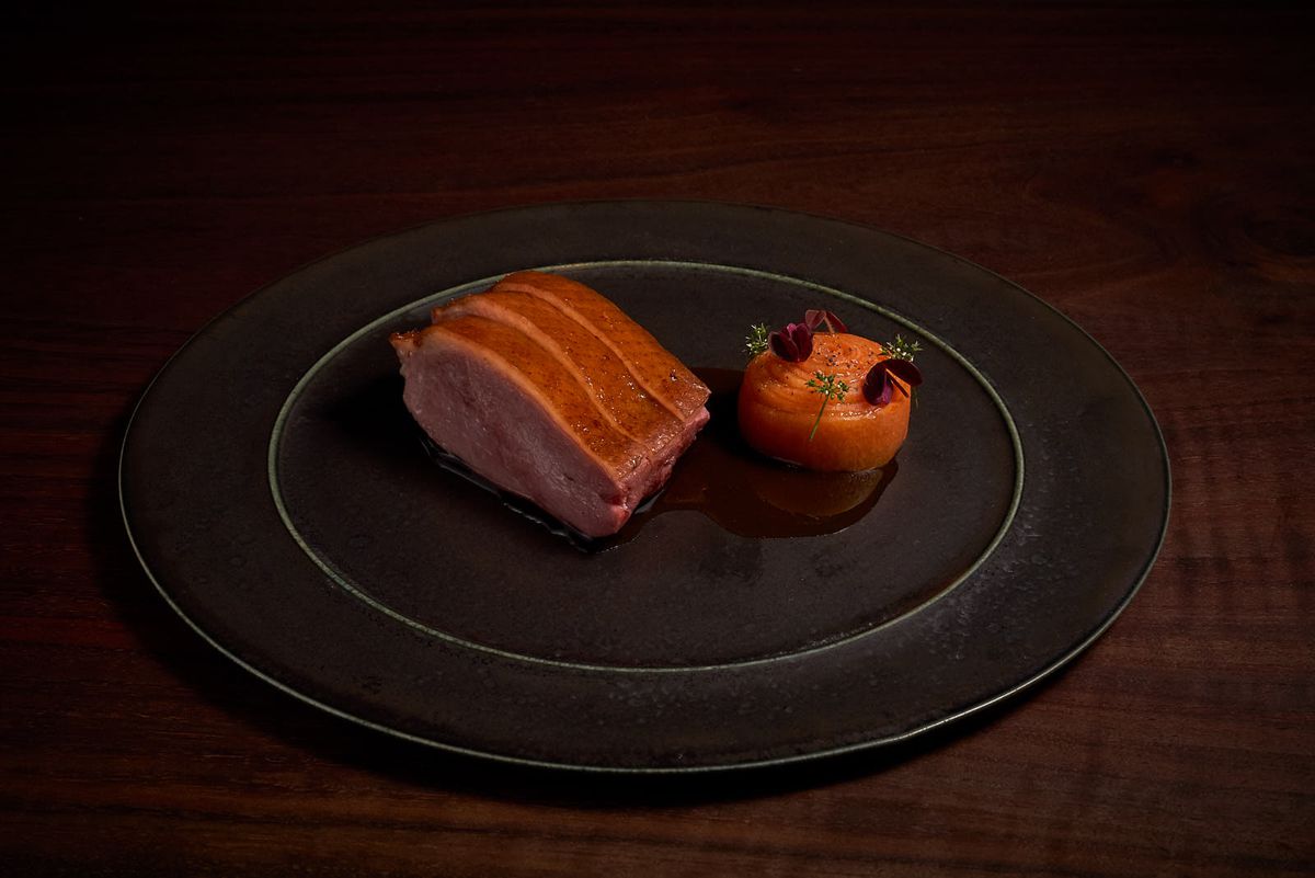 An order piece of sliced duck is arranged on a granite plate in a low-lit photograph.