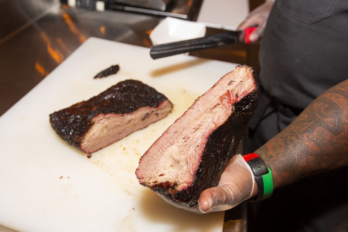 A man's hand holds a slab of smoked meat.