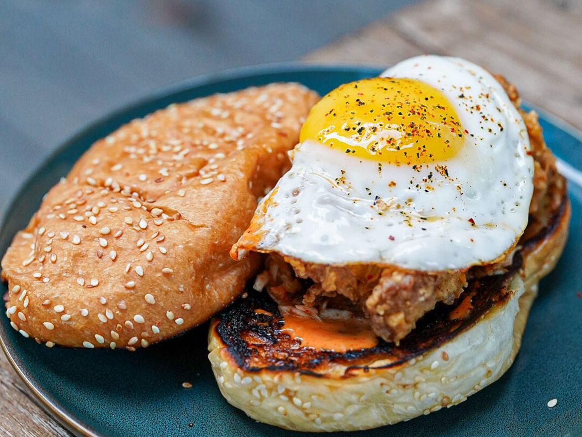 An open fried chicken sandwich on a long sesame seed bun topped with a fried egg