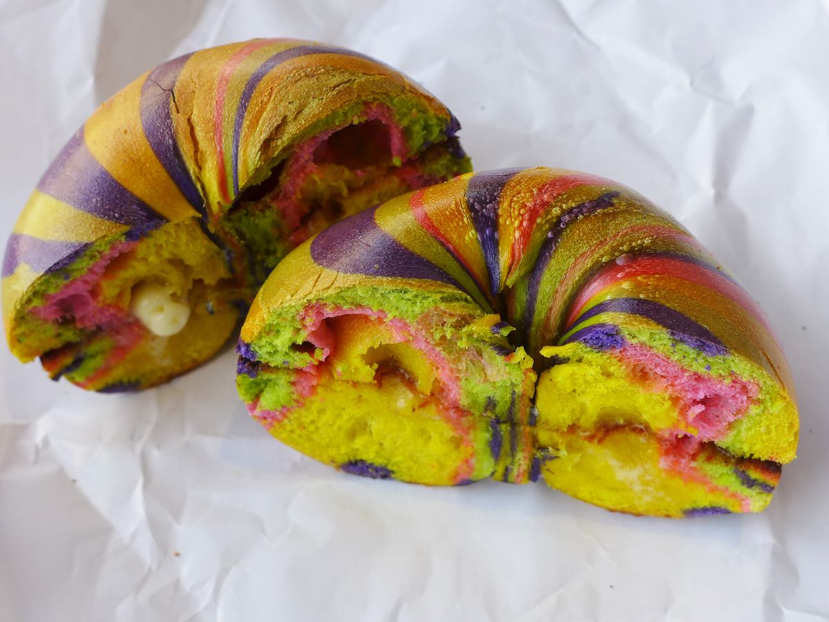 A bagel buttered and cut in half, with a rainbow pattern on its convex surfaces.