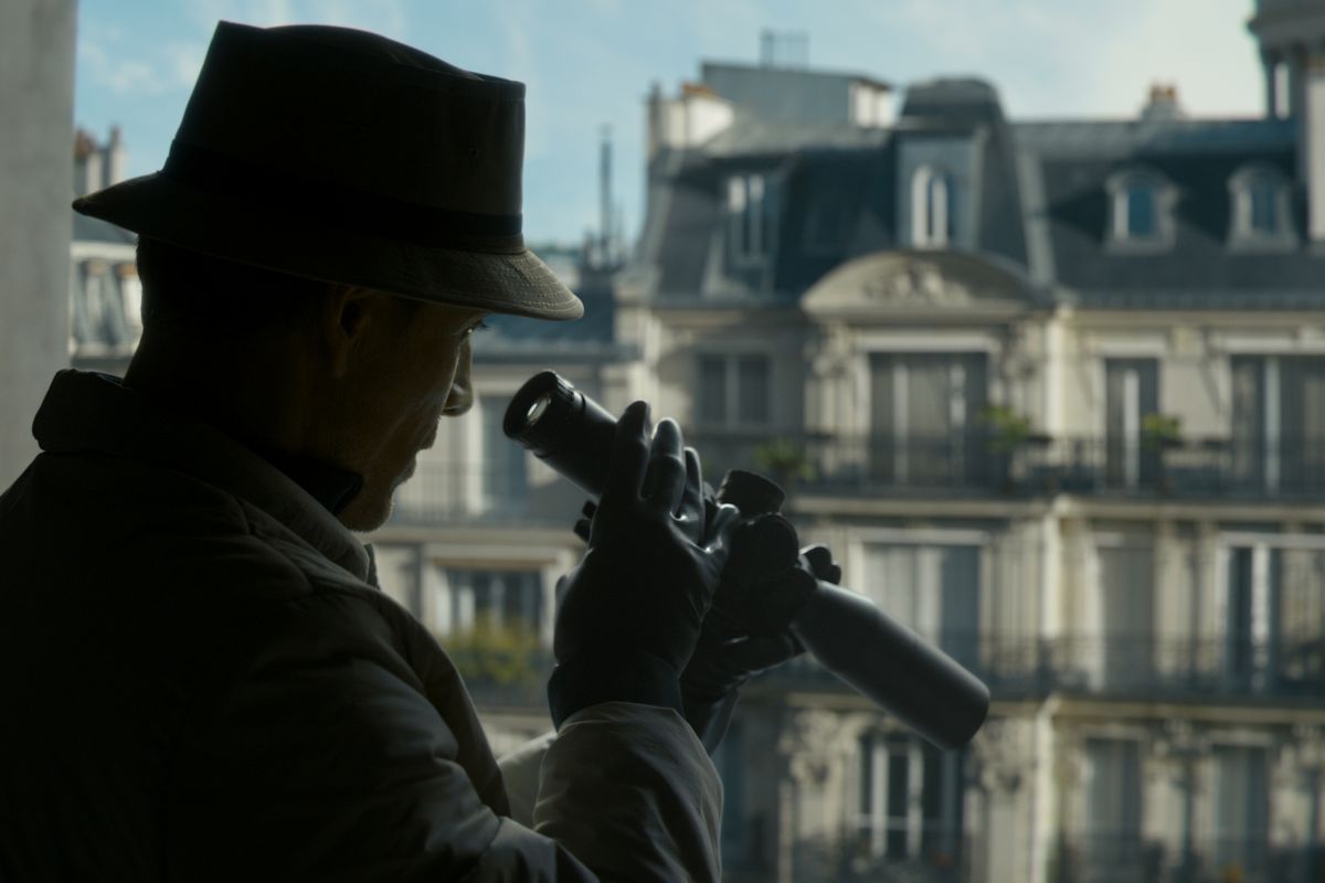Michael Fassbender as an assassin peering through a sniper scope in a window in The Killer.