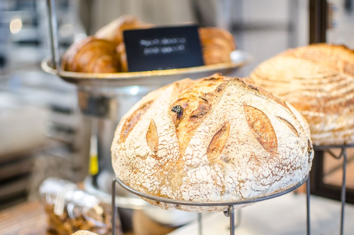 Sourdough breads are displayed in a bakery, with croissants visible in the background