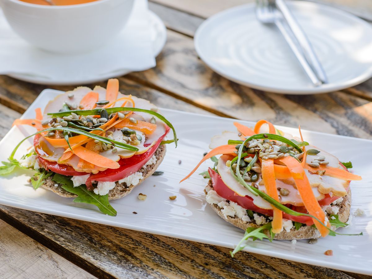 Two canapes sit on a long plate topped with cheese, arugula, shaved carrots, and other vegetables and pepitas