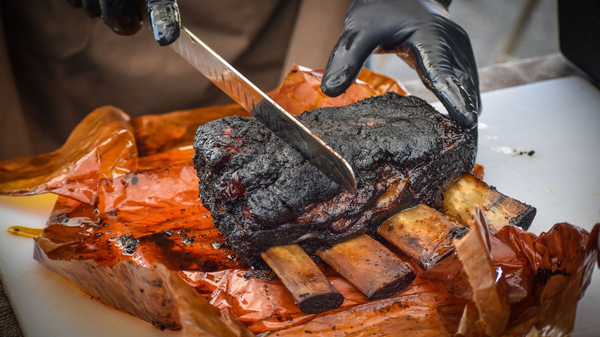 Hands in black gloves cut through a rack of wide beef ribs from a pop-up barbecue restaurant, Axiom Kitchen.